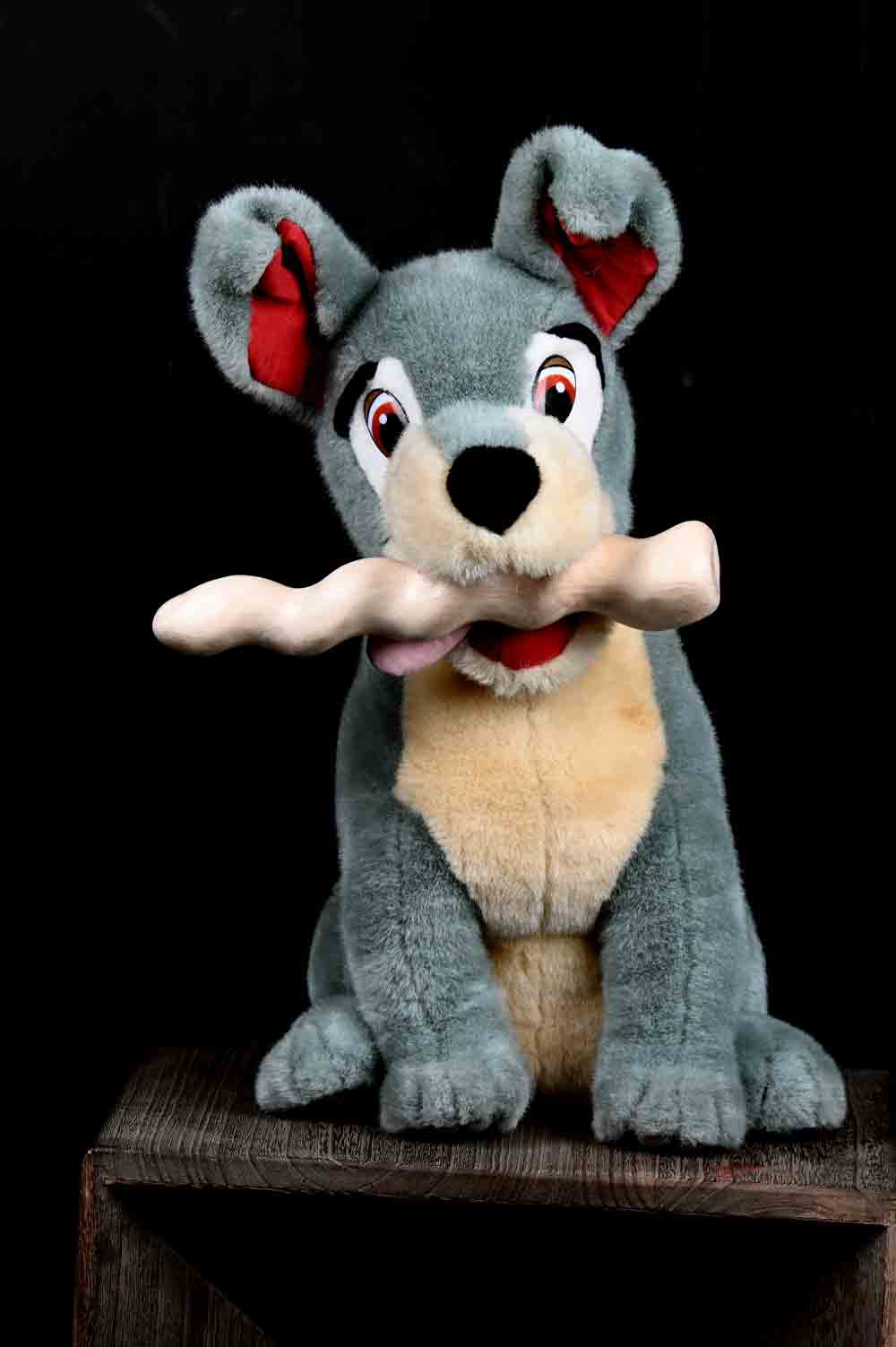 Graues Plüsch-Hundespielzeug mit einem Holzobjekt im Maul vor schwarzem Hintergrund