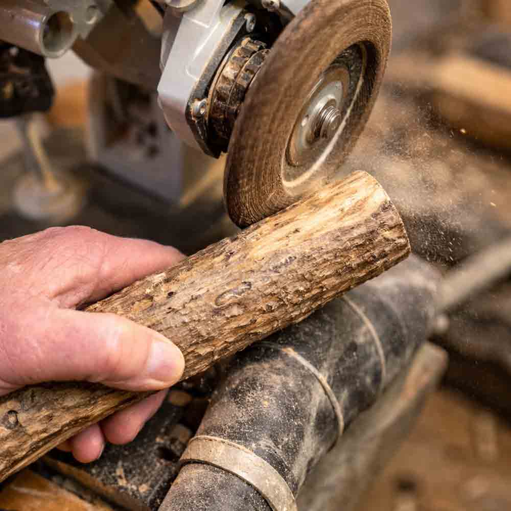 Hand schleift einen naturbelassenen Holzrohling mit einem rotierenden Schleifwerkzeug in der Werkstatt.